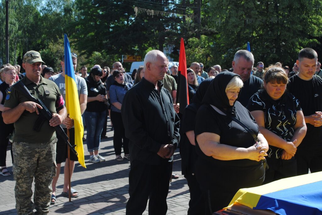 Люди з прапорами на похоронній церемонії.