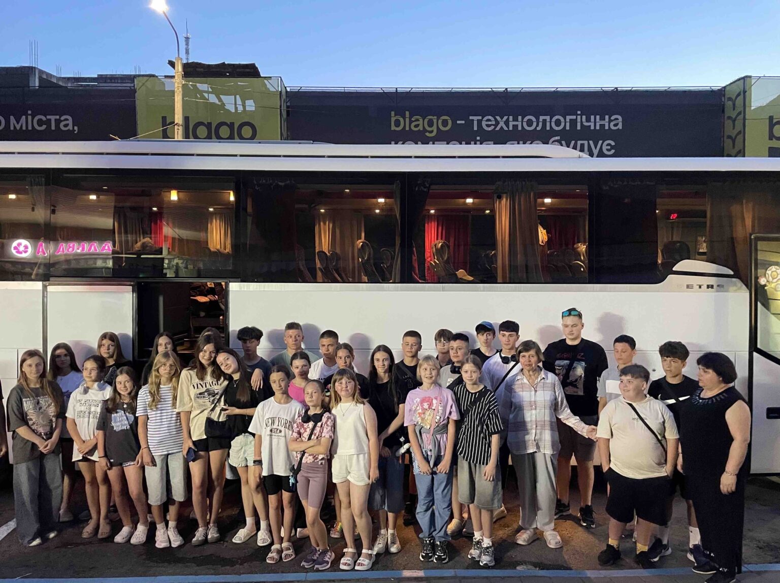 Група людей перед автобусом на заході сонця.