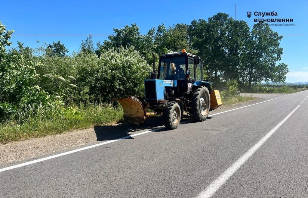 Трактор працює на сільській дорозі біля лісу.