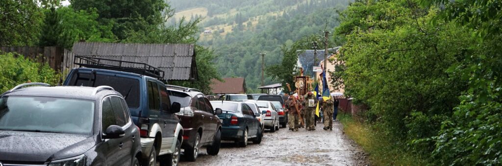 Похоронна процесія серед автомобілів та дерев у селі.