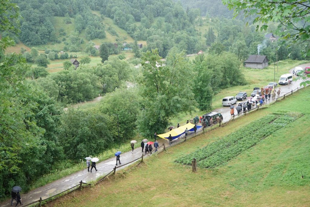 Люди з парасольками йдуть селом під дощем.
