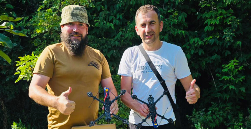 Двоє чоловіків стоять з дронами на природі.