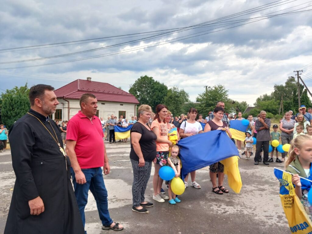 Люди на вулиці з українськими прапорами й кульками.