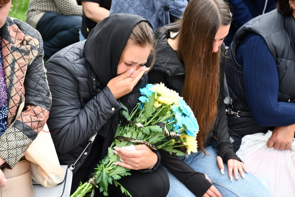 Жінка плаче з букетом квітів на колінах