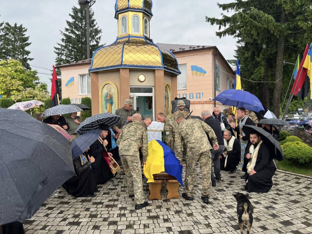 Військові і священики під дощем біля каплиці.