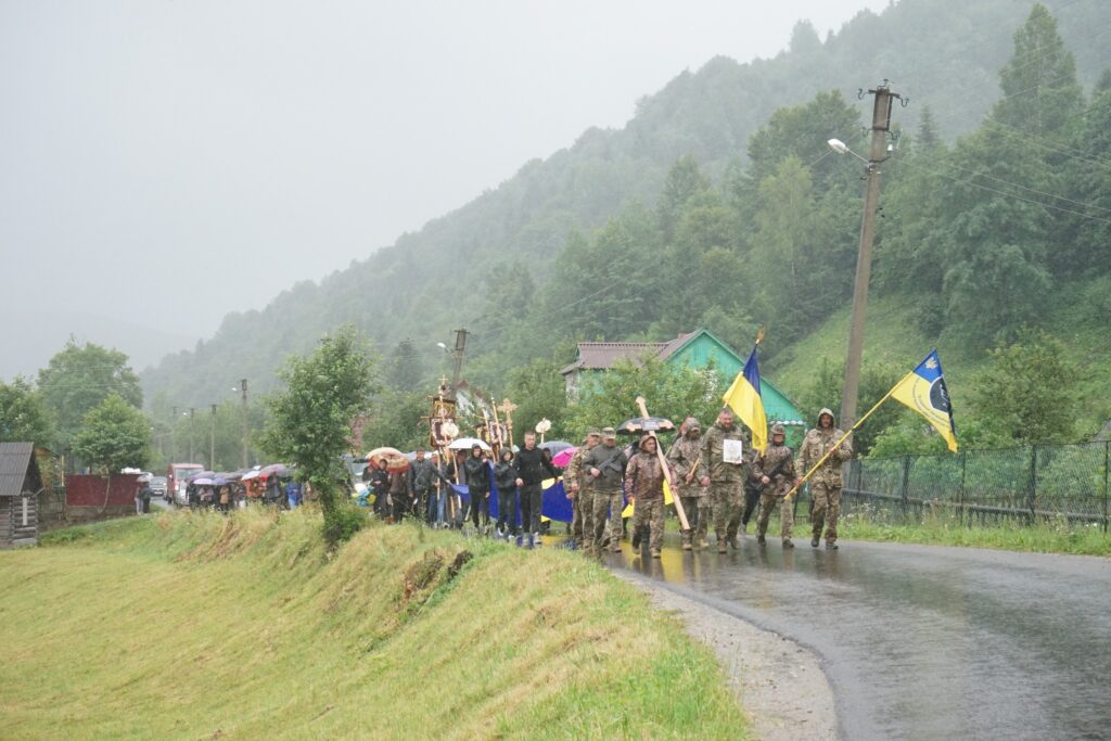Хода людей з прапорами під дощем у Карпатах.