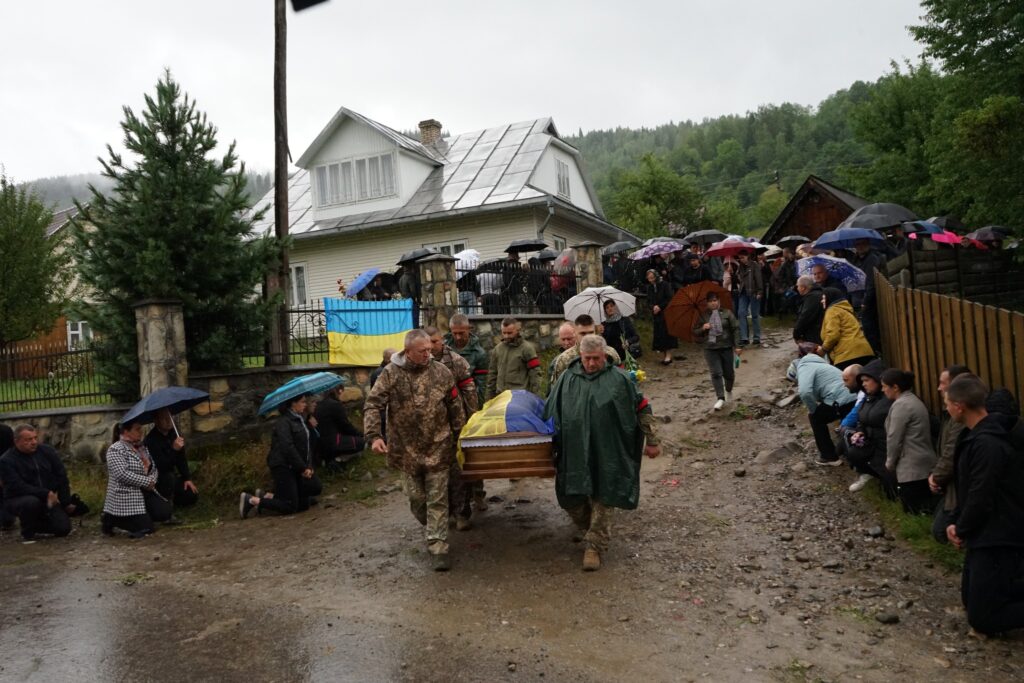Похоронна процесія під дощем у селі.