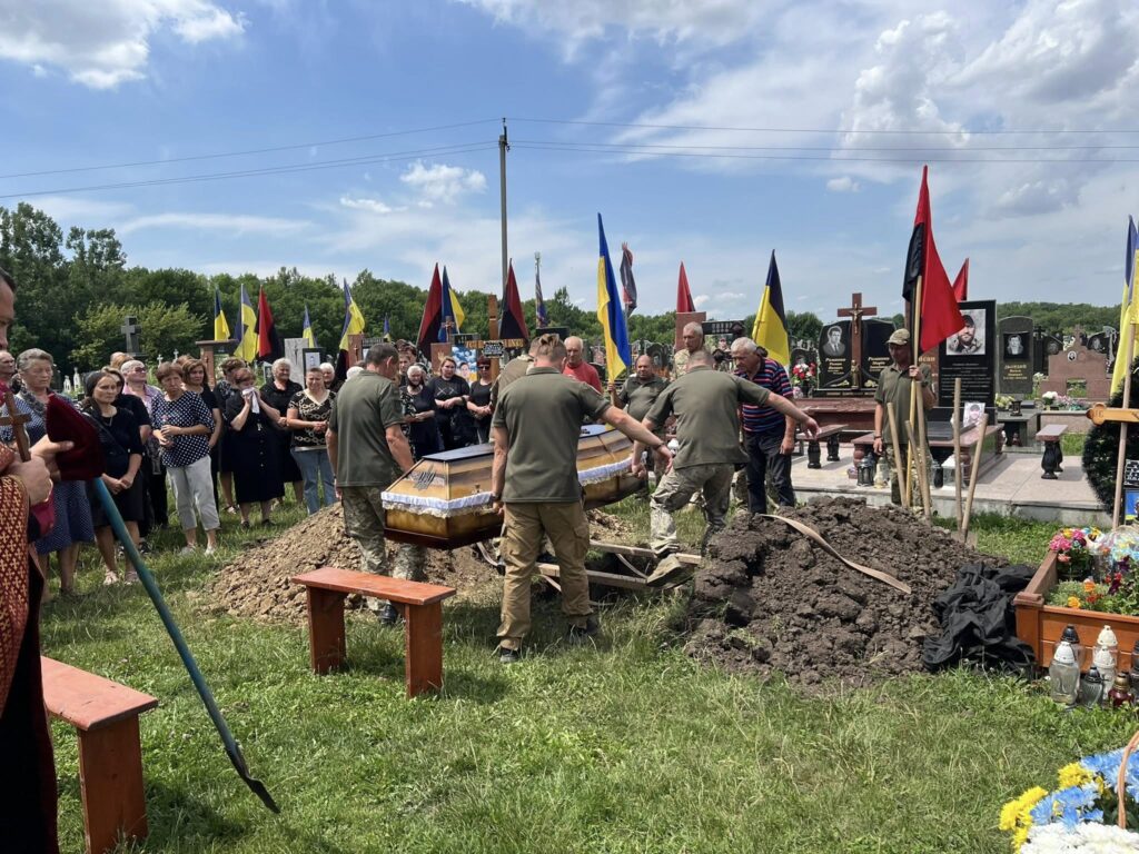 Прощання на кладовищі з українськими прапорами.