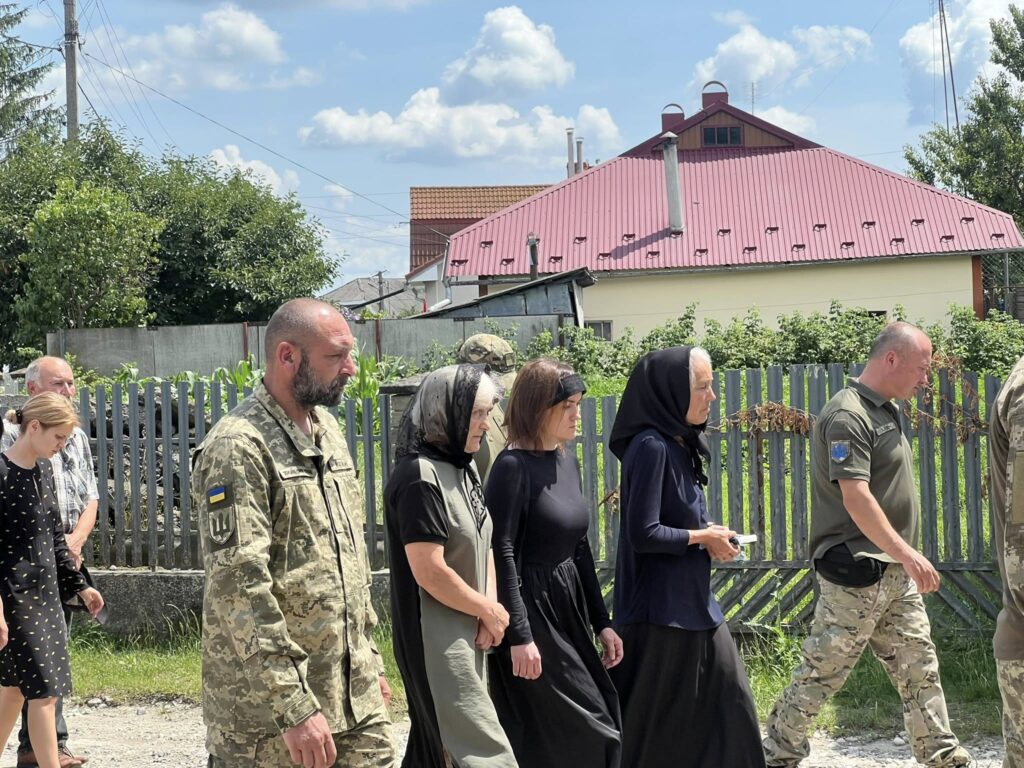 Люди йдуть біля сільського паркану під сонцем.