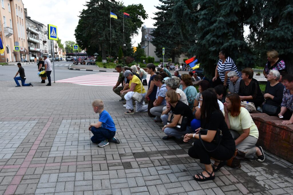 Люди навколішки на площі з прапорами України.