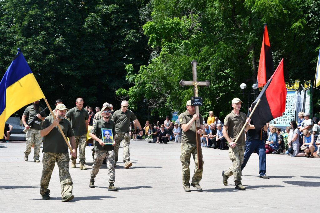 Парад військових з прапорами та фотографією.