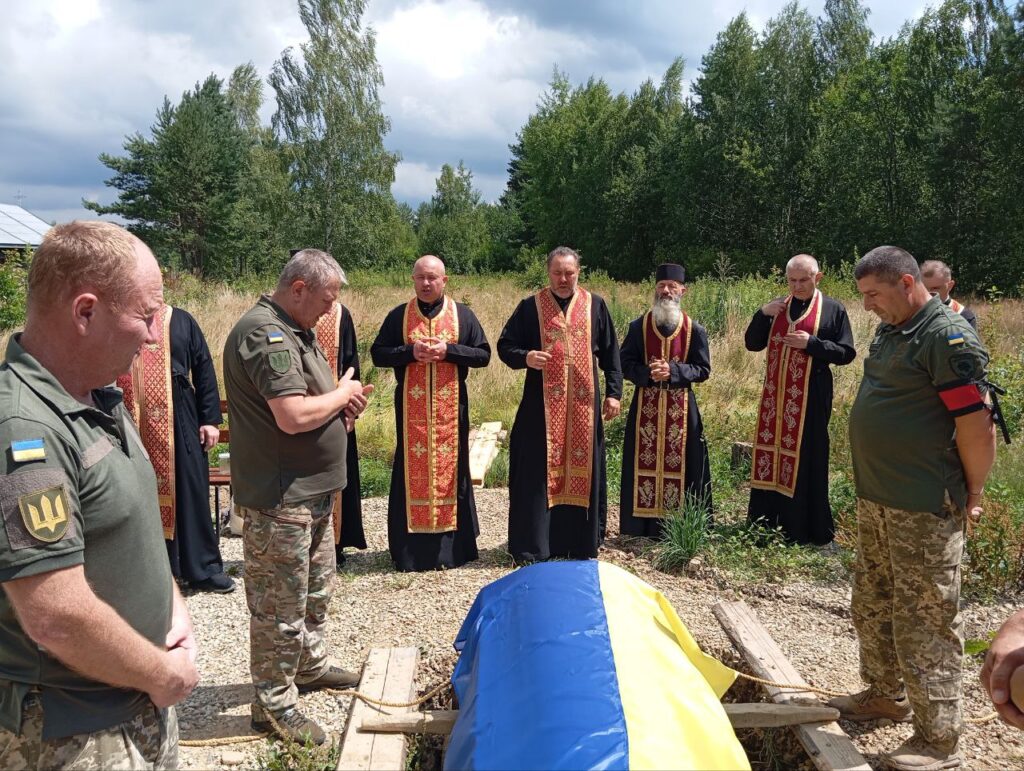 Військове вшанування із священиками, прапор на труні.