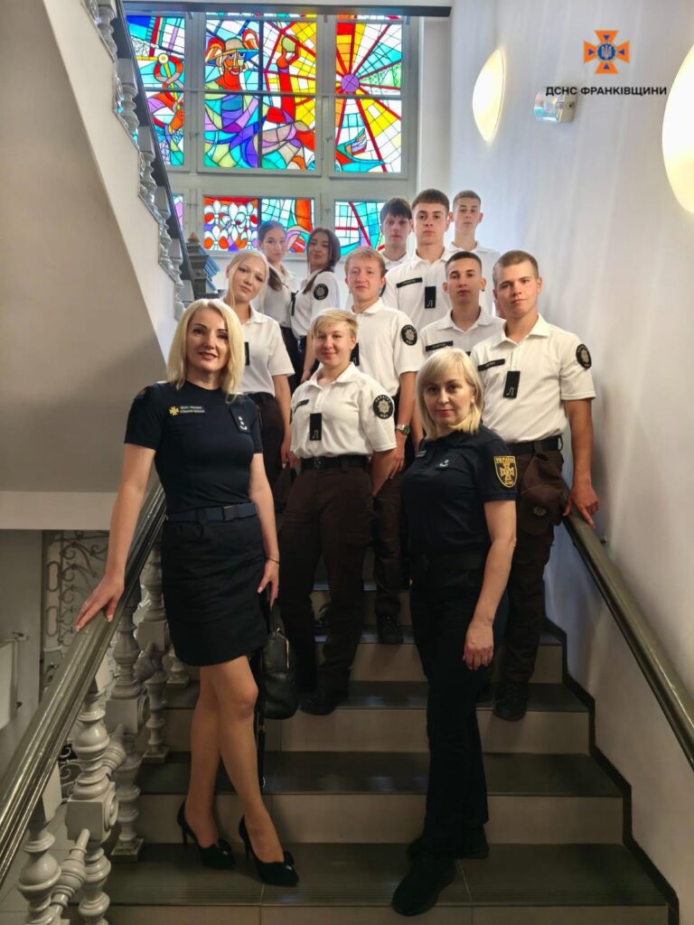 Група людей на сходах перед вітражем.