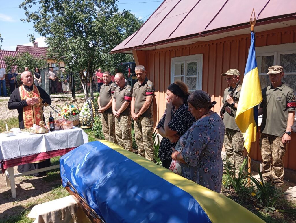 Поховання військового з прапором, священик читає молитву.