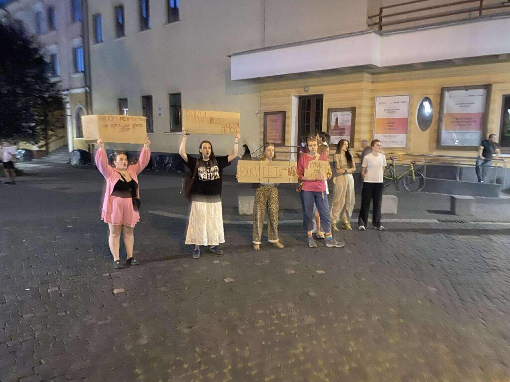 Протест на вулиці, учасники тримають плакати ввечері.