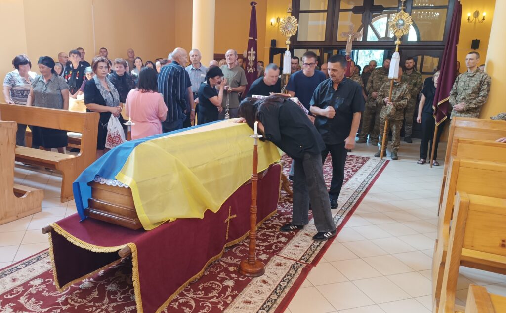 Люди прощаються з покійним у церкві, труна з прапором.