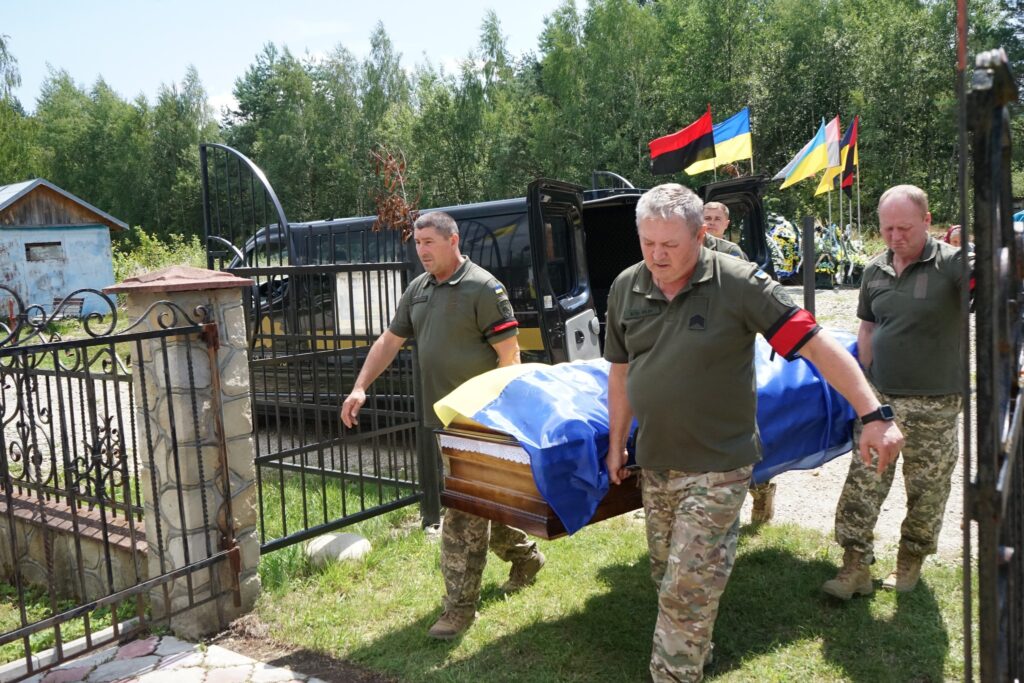 Військові несуть труну, покриту прапором України.