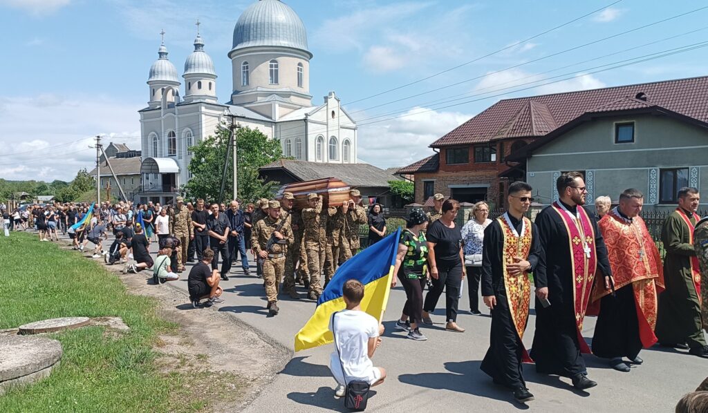 Церковна процесія з жовто-синім прапором, натовп людей.