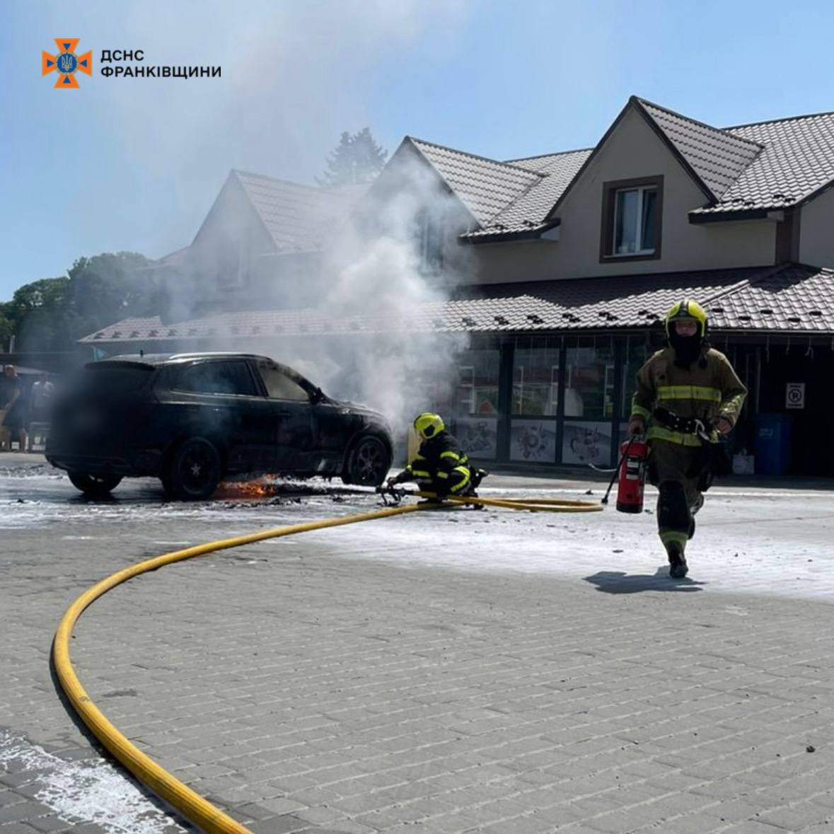 Пожежники гасять автомобіль біля будівлі.