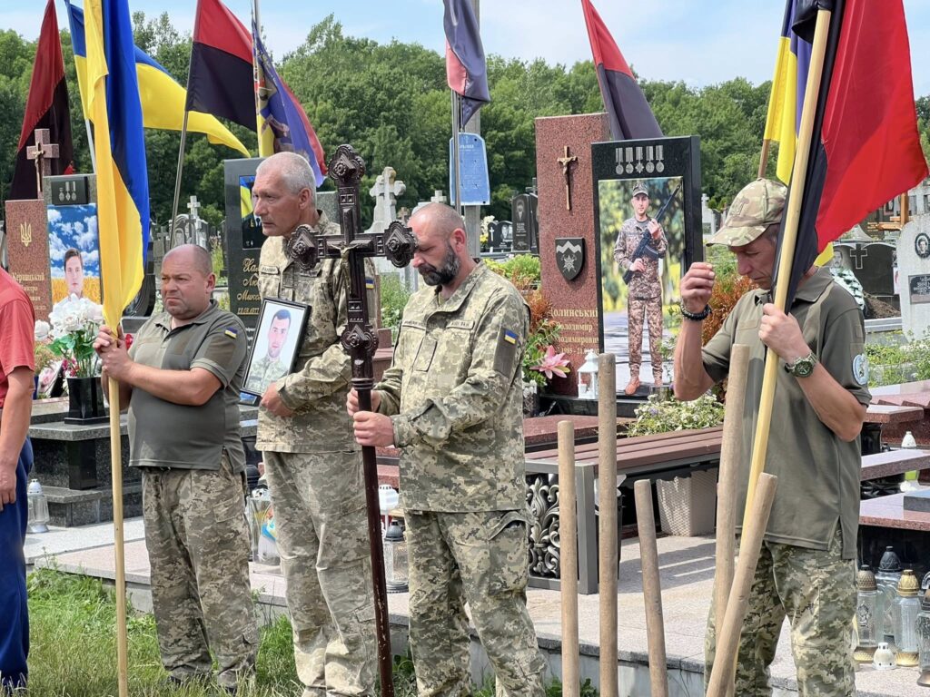 Люди з прапорами на військовому кладовищі.