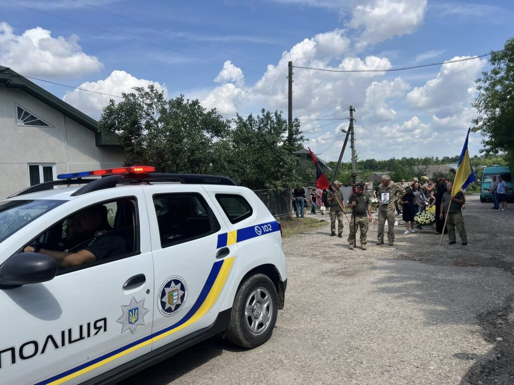 Поліцейський автомобіль та процесія з прапорами на вулиці.