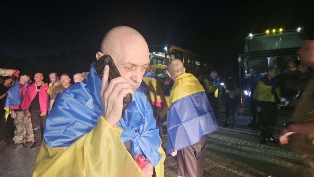 Люди в українських прапорах розмовляють біля автобусів