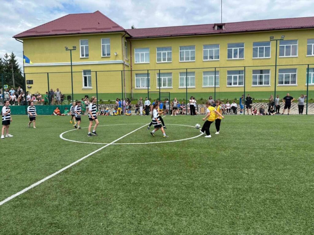 Діти грають у футбол на шкільному стадіоні.