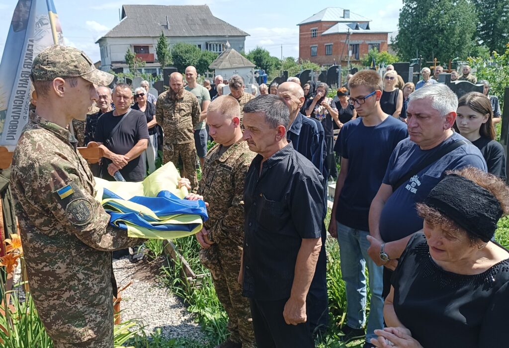 Військовий з прапором на похороні в Україні.