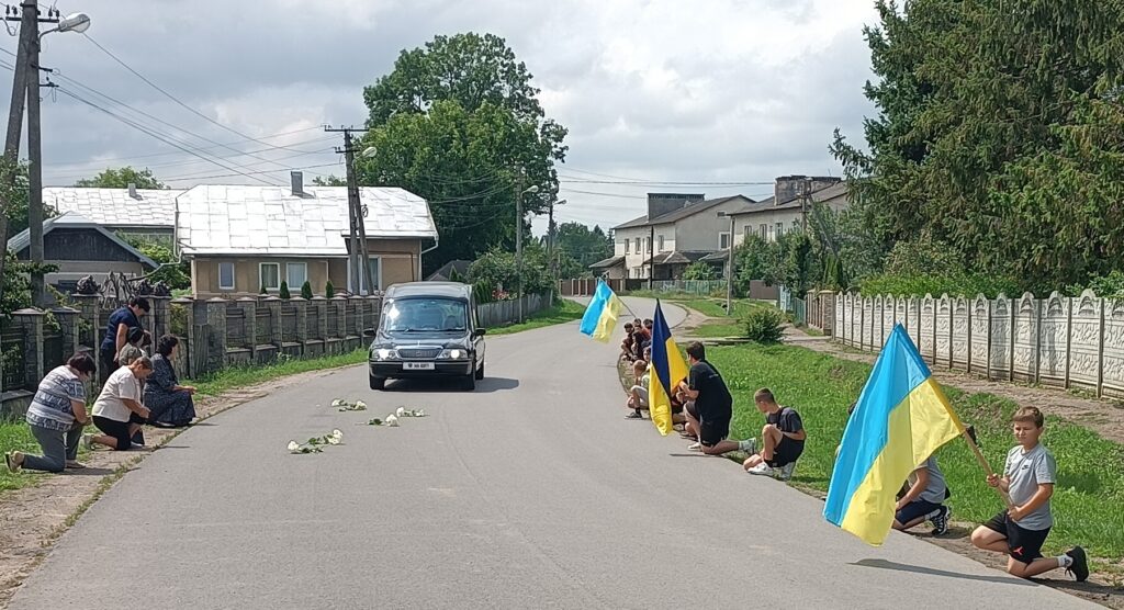 Жителі вшановують похоронну процесію на дорозі.