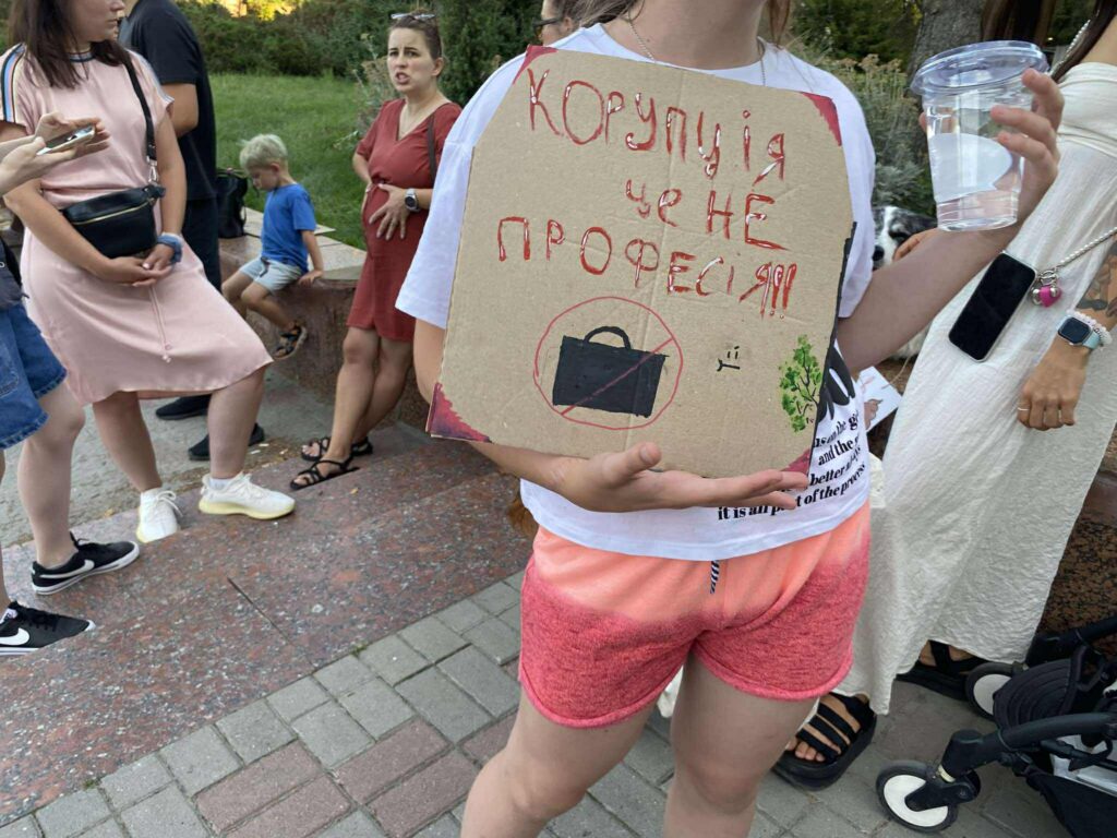 Люди на протесті тримають плакат проти корупції.