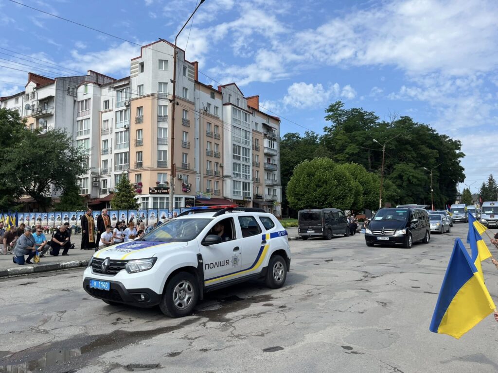 Автоколона поліції на міській вулиці, прапори України.