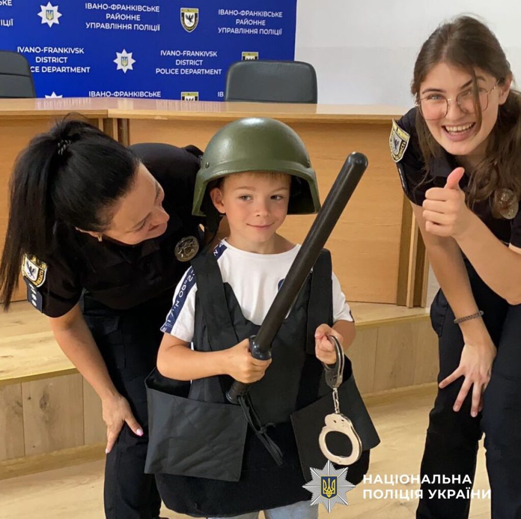 Дитина в поліцейському обладунку з офіцерами поліції.