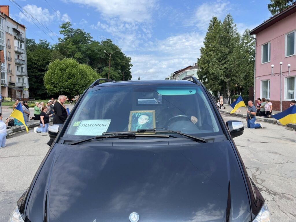Похоронний кортеж з українськими прапорами на вулиці.