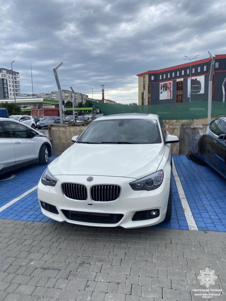 Біле авто на парковці під хмарним небом.
