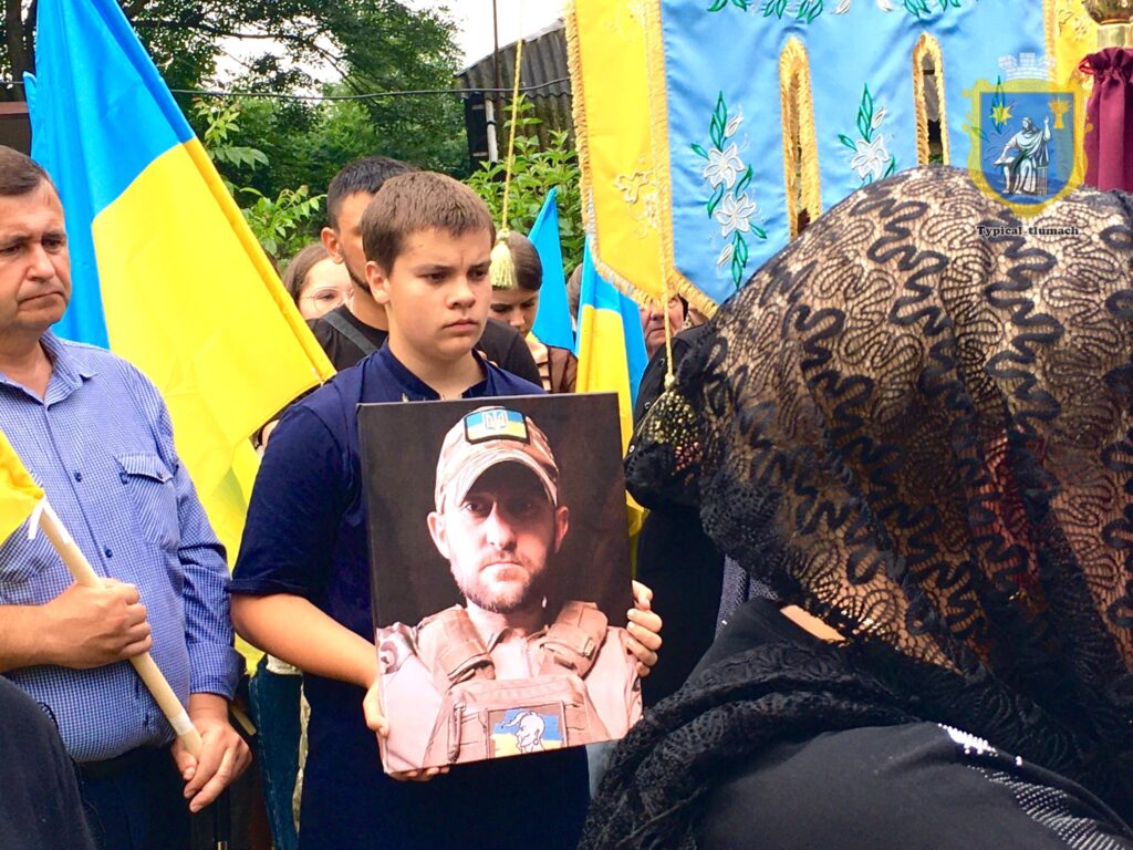 Люди на похороні з портретом військового героя.