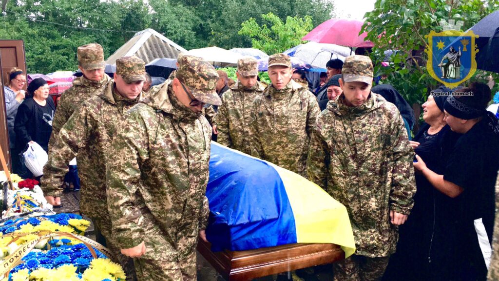 Військові прощаються з прапором України під дощем.