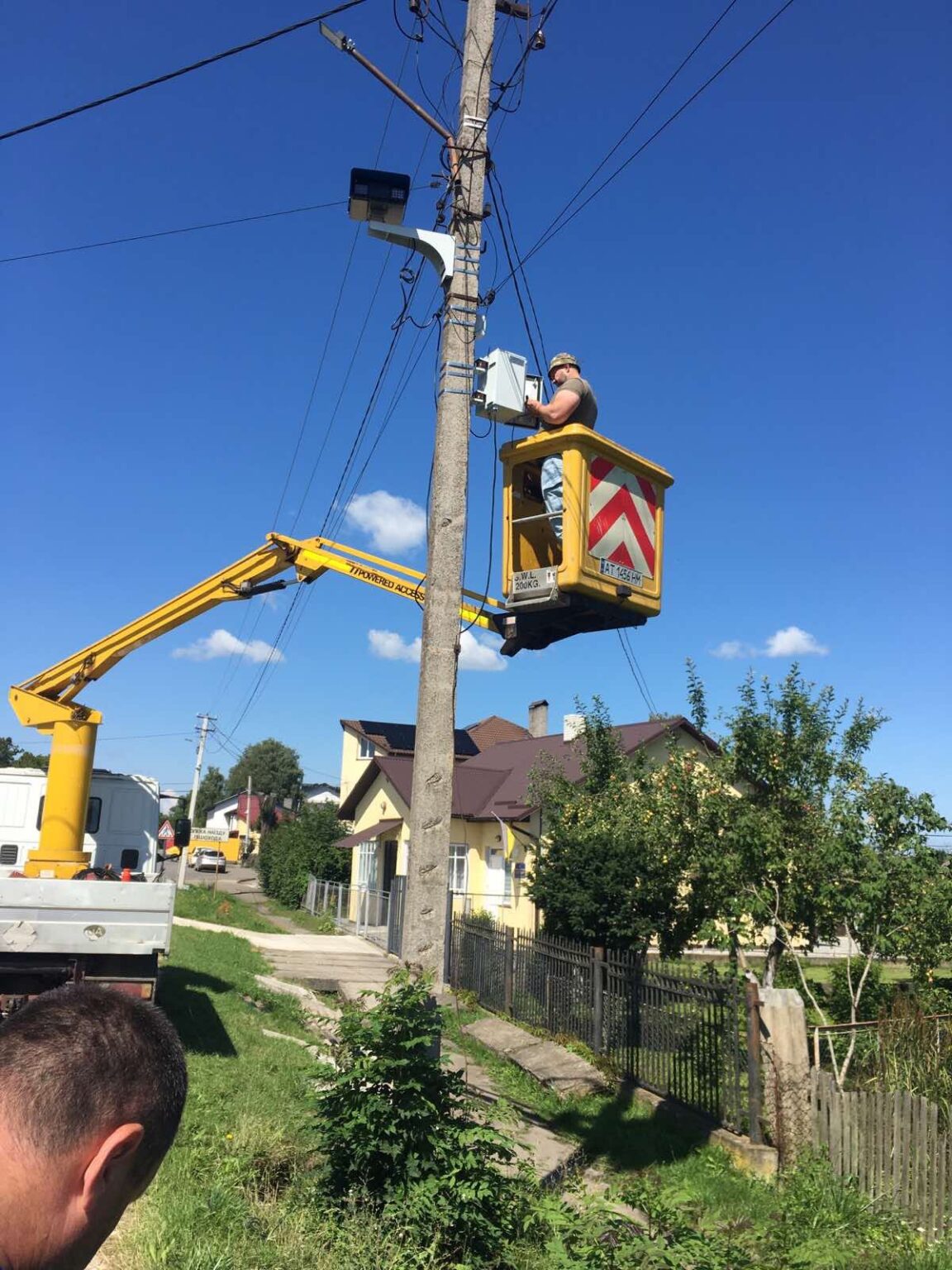 Робітник ремонтує електролінію на підйомнику, сонячний день.