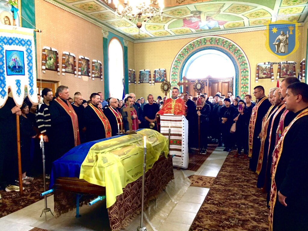Поминальна служба у церкві з труною під прапором.