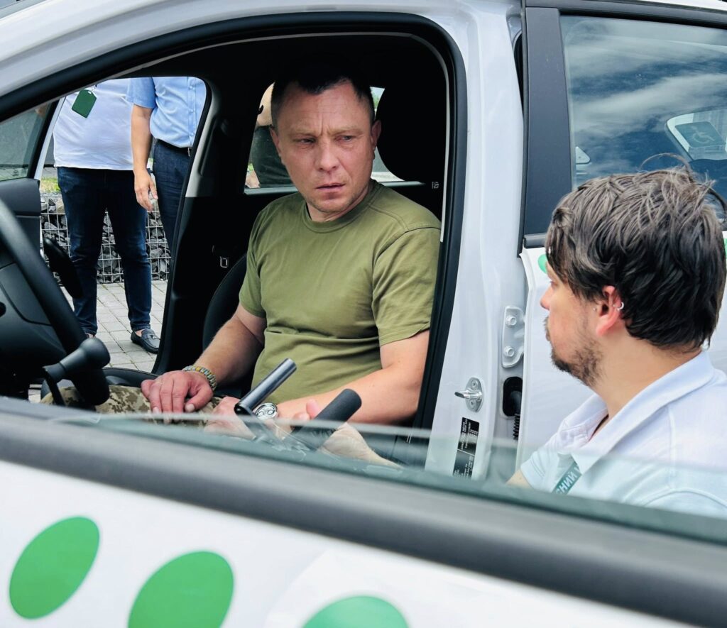 Двоє чоловіків спілкуються в автомобілі на вулиці.