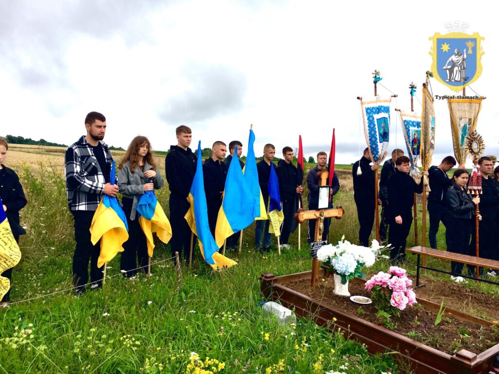 Люди з прапорами біля могили на полі.