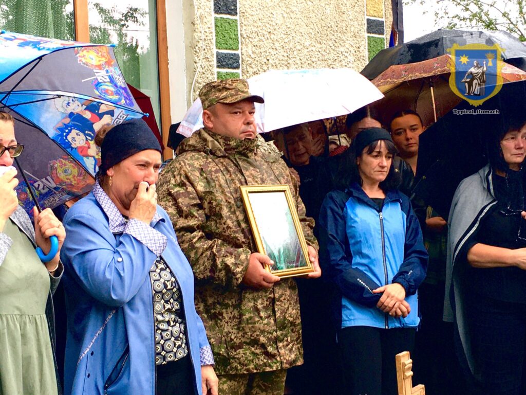 Люди під дощем на прощанні з військовим.