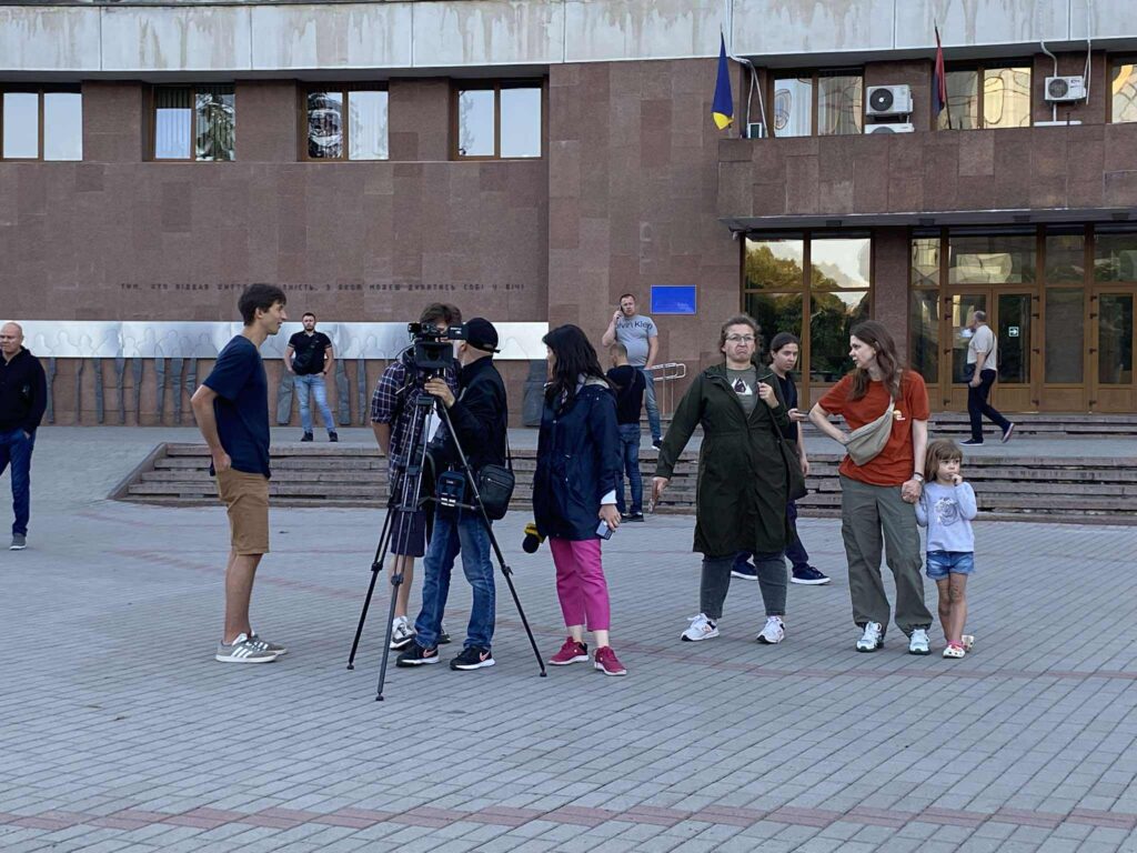 Люди збираються перед будівлею, знімається інтерв'ю.