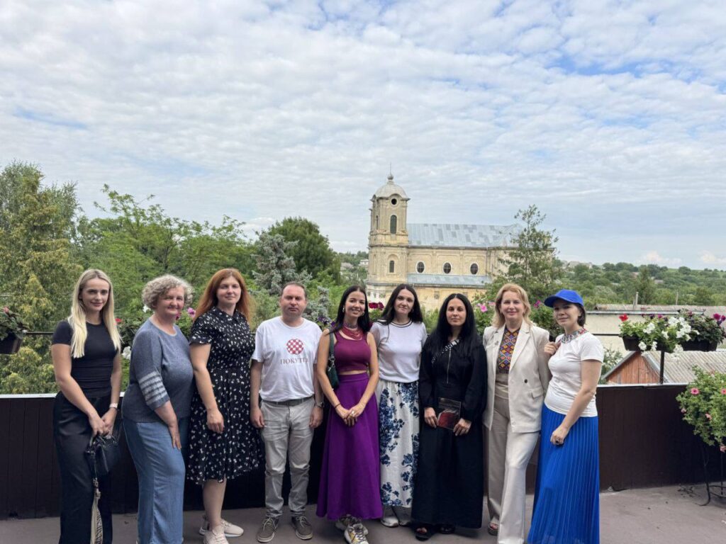 Група людей позує на тлі церкви та природи.