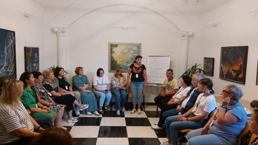 Люди обговорюють на зустрічі в кімнаті з картинами.