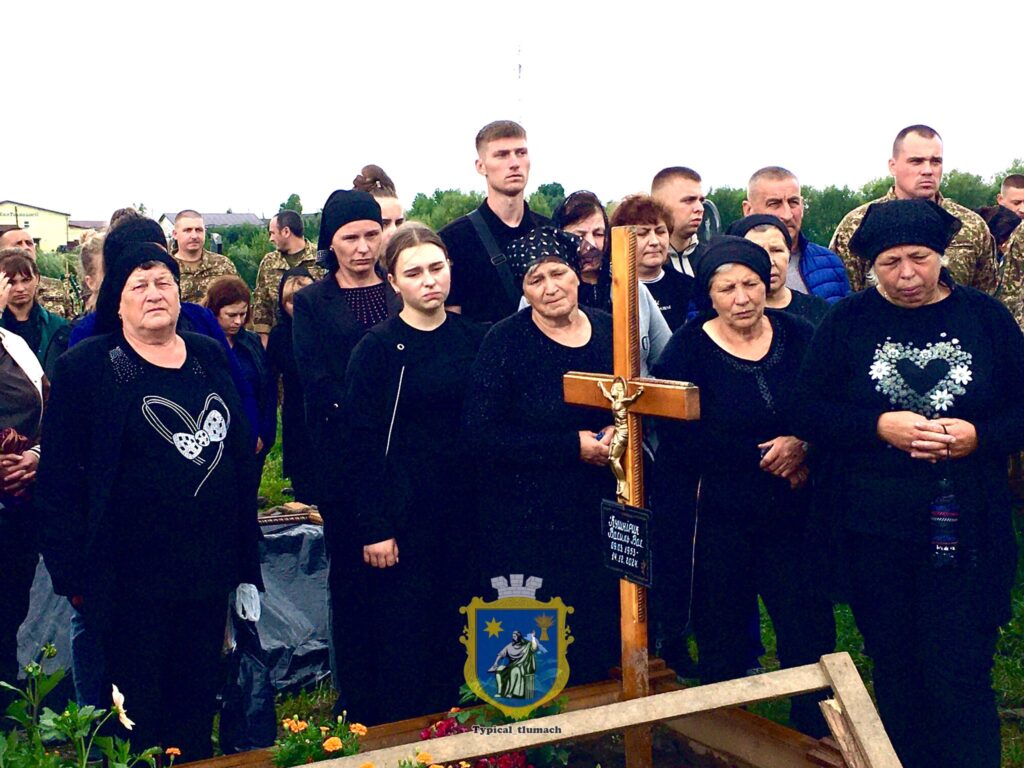 Люди на похороні біля хреста на кладовищі.