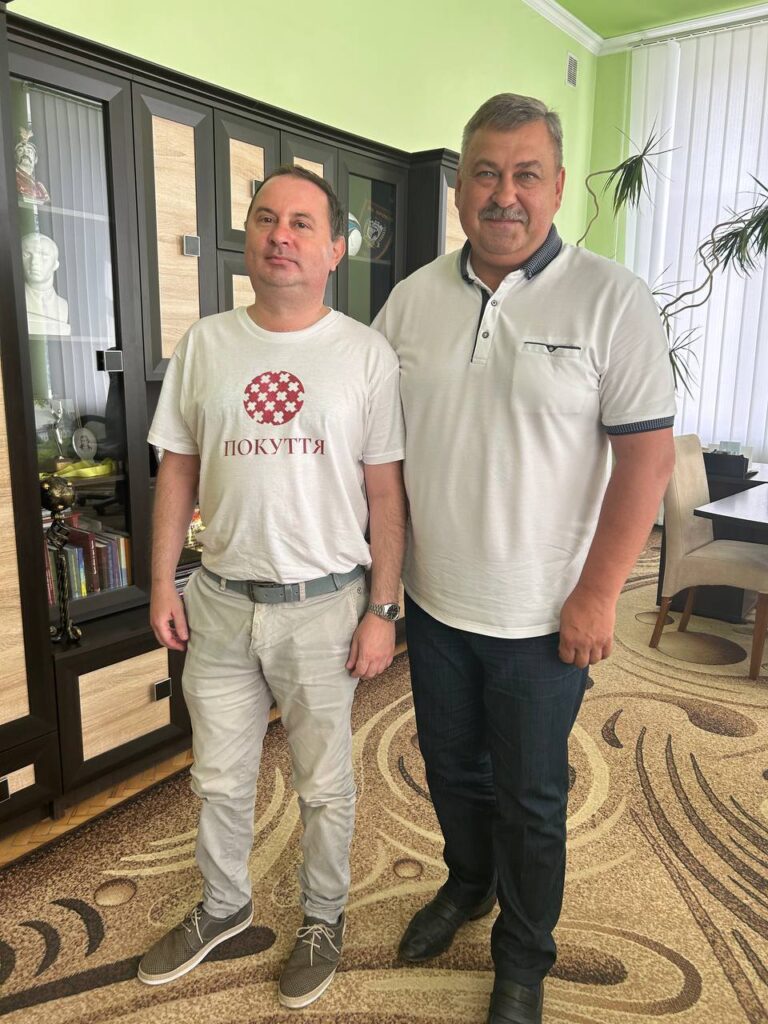 Двоє чоловіків стоять перед книжковою шафою.