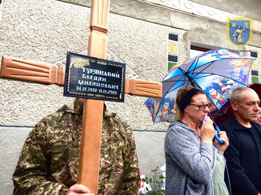 Люди біля хреста з дощем і парасольками.