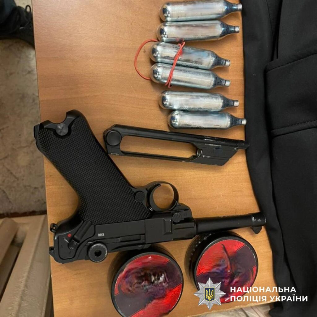 Пістолет, балони та інші предмети на столі.