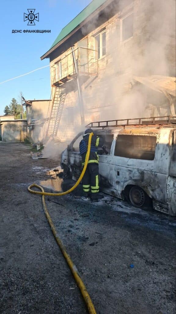 Пожежник тушить палаючий автомобіль біля будинку.