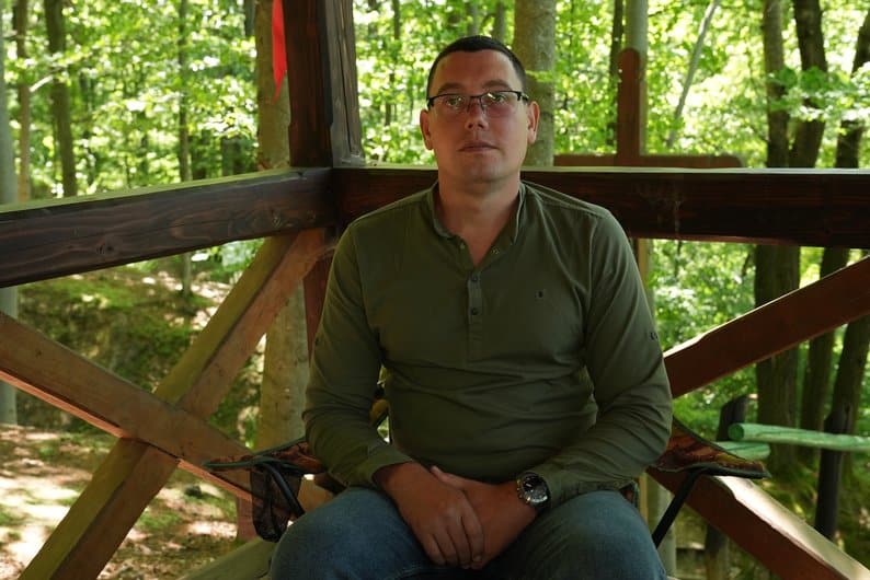 Чоловік на дерев'яній платформі в зеленому лісі.